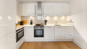 Een moderne keuken met witte kastjes, een ingebouwde oven en een aanrecht met een koffiezetapparaat en andere apparaten.