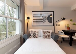 Quarto de hotel moderno com uma cama grande, uma escrivaninha e um vaso de planta.
