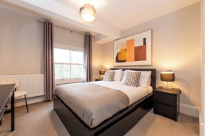 Ein Schlafzimmer mit Bett, Nachttischen, Schreibtisch und einem Fenster mit Vorhängen.