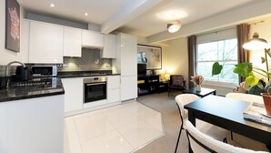 A modern kitchen with white cabinets, a black countertop, and a dining area with a table and chairs. - Stunning 1 BR Surbiton with views, near station - Pass the Keys (Surbiton)