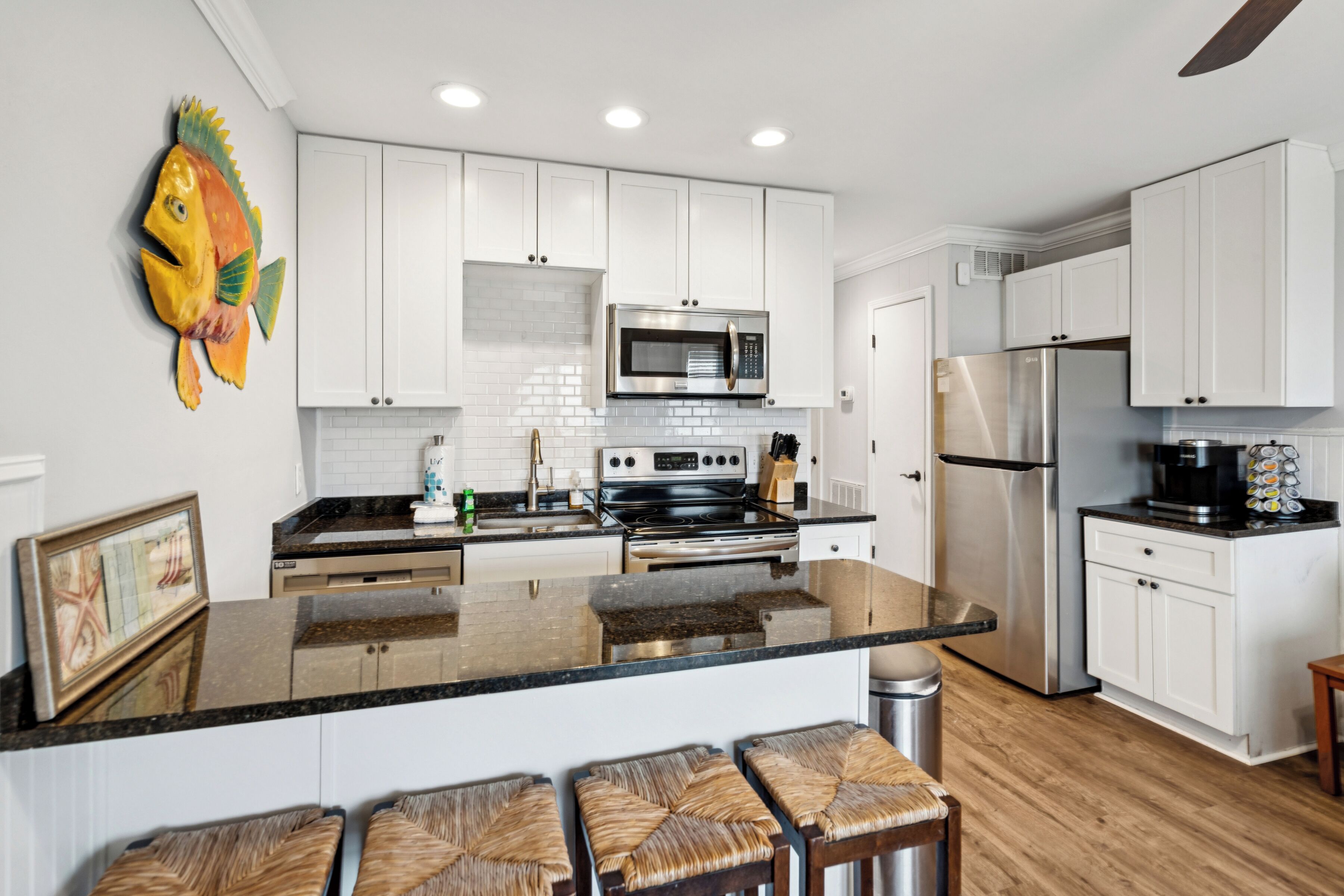 A modern kitchen with white cabinets, a stainless steel refrigerator, a microwave, and a large island with bar stools.