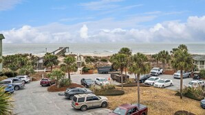Ein Parkplatz mit verschiedenen Autos, im Hintergrund ein Strand und Palmen.