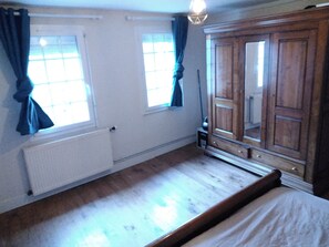 Ein Schlafzimmer mit einem hölzernen Bett, zwei mit Vorhängen versehenen Fenstern, einem Heizkörper und einem Kleiderschrank.