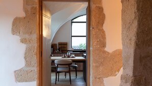 Un couloir aux murs en pierre apparents mène à une cuisine dotée d’un plancher en bois et d’une fenêtre qui laisse entrer la lumière naturelle.