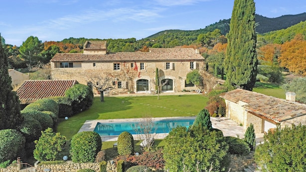Une villa en pierre dotée d’une piscine, entourée de jardins bien entretenus et avec une chaîne de montagnes en toile de fond.