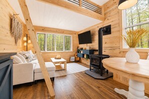 LâintĂ©rieur dâun chalet accueillant, avec un canapĂ©, une table, une cheminĂ©e et un tĂ©lĂ©viseur fixĂ© au mur.