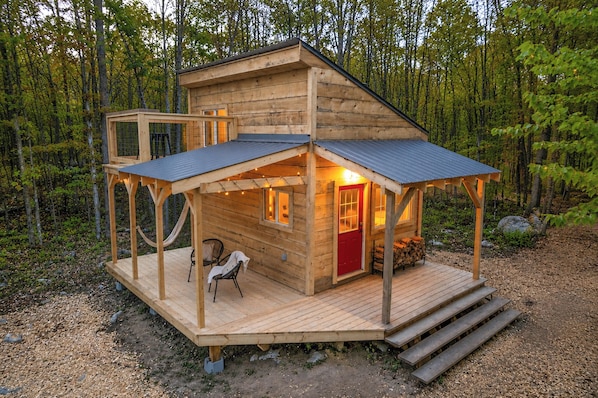 Une cabane en bois avec une véranda, une porte rouge et un hamac.