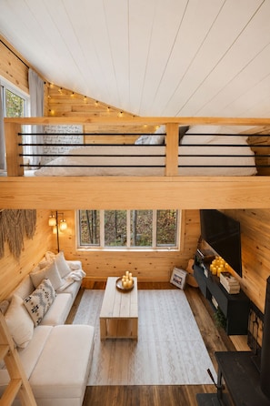 Un intérieur de chalet chaleureux avec un lit en mezzanine, un canapé, une table basse et une cheminée.