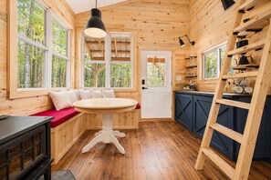 LâintĂ©rieur dâun chalet en bois comprend une table ronde, des bancs, un coin cuisine et de grandes fenĂȘtres.