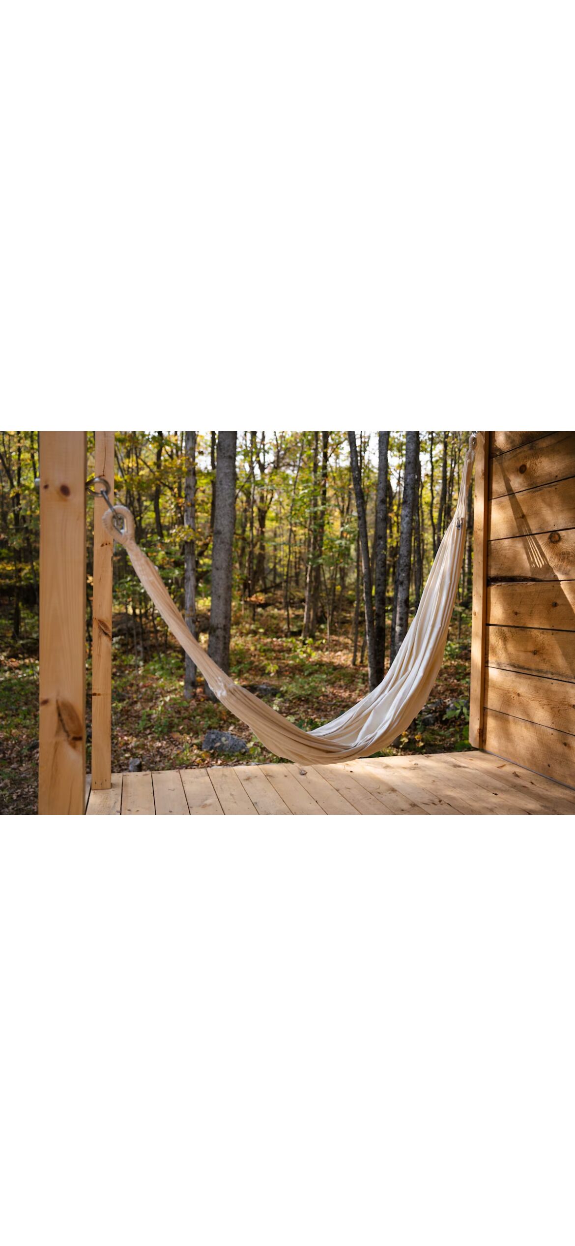 A hammock suspended between wooden beams in a forested area with a wooden deck.