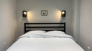 Una cama bien hecha con un edredón a rayas, dos lámparas de lectura fijadas a la pared y luces empotradas en el techo.