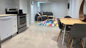 Una cocina moderna con horno y microondas integrados, un comedor con mesa y sillas de madera, y una sala de estar con sofá y alfombra colorida.