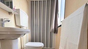 A narrow bathroom with a white sink, toilet, and striped shower curtain. - Gargano Private Experience in the Heart of the Gargano - Nature & Sea (Villaggio Moresco Basso)