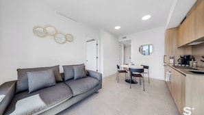 Ein modernes Wohnzimmer mit grauem Sofa, einem Essbereich mit Tisch und Stühlen sowie einer Küche mit Holzausstattung und Spüle.