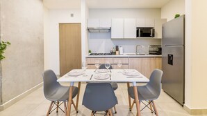 A modern kitchen with white cabinets, a stainless steel refrigerator, and a dining area with a table set for four. - Arena Calzada (Monterrey)