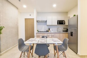 A modern kitchen with white cabinets, a stainless steel refrigerator, and a dining area with a table set for four. - Arena Calzada (Monterrey)