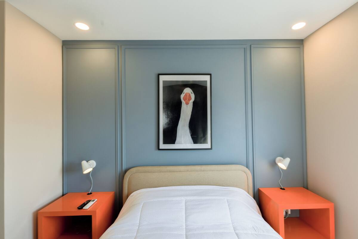 A bedroom with a bed, two nightstands, a framed picture on the wall, and a ceiling light.