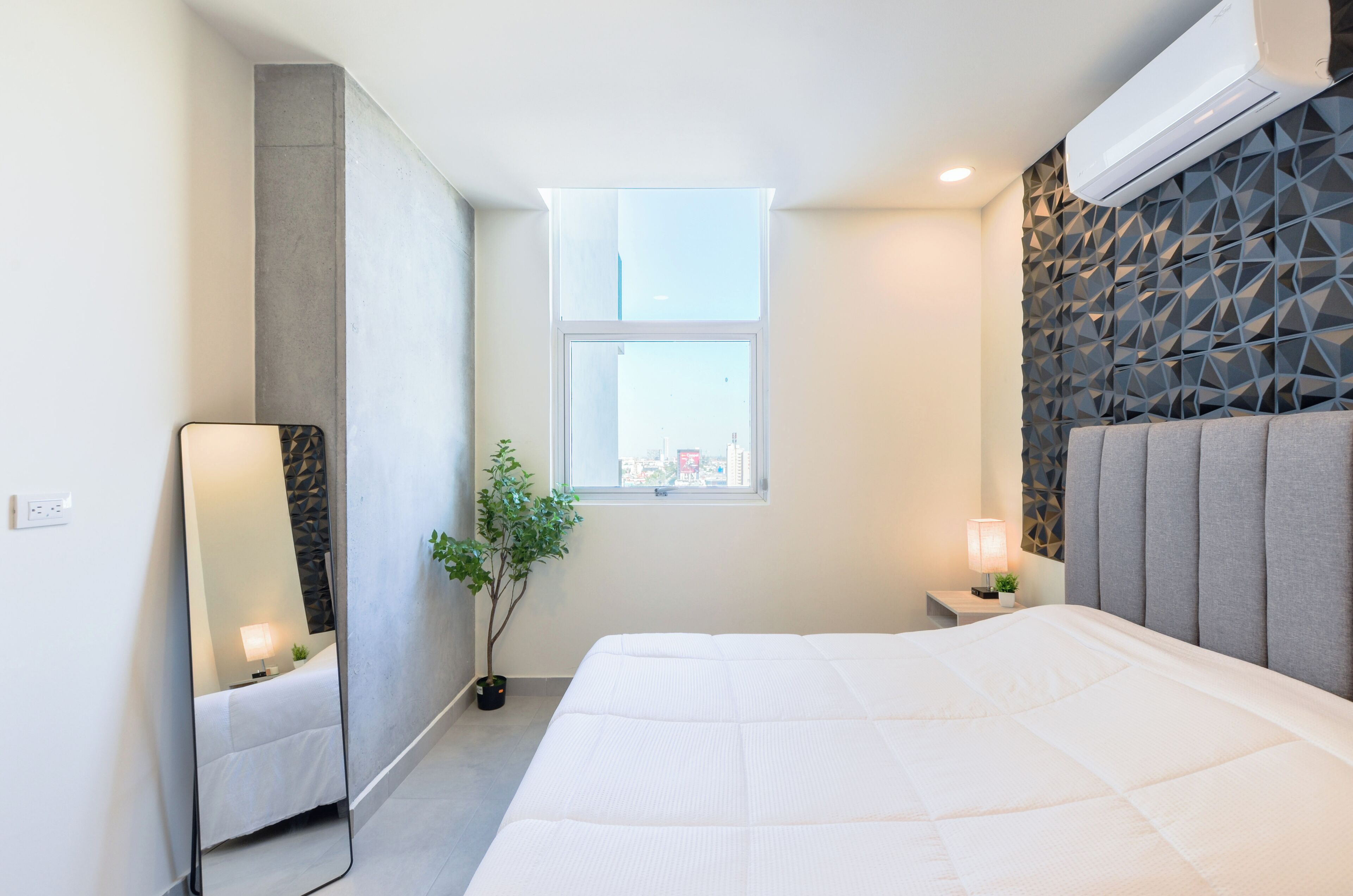 Un dormitorio moderno con una cama grande, una ventana, un espejo y una mesita de noche con lámpara.