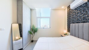 A modern bedroom with a large bed, a window, a mirror, and a nightstand with a lamp. - Arena Calzada (Monterrey)