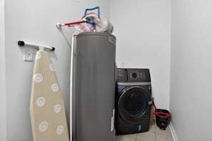 Un área de lavandería compacta con lavadora, calentador de agua alto y una tabla de planchar.