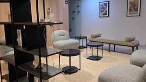 Uma sala de estar moderna com uma estante preta, um sofá cinzento, uma mesa de centro redonda e um banco.