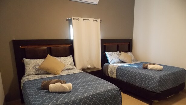 Twee eenpersoonsbedden met beddengoed met een patroon, een gordijn en een wandairconditioner.