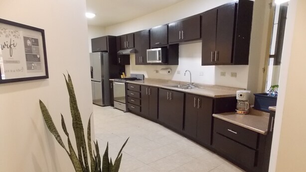 A modern kitchen with dark cabinets, a stainless steel refrigerator, a microwave, and a coffee maker.