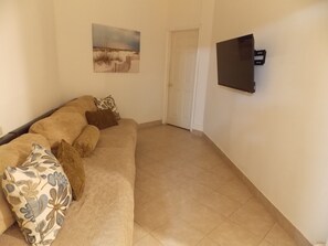 A living room with a beige sofa, patterned pillows, a framed picture on the wall, and a flat-screen TV mounted on the wall.