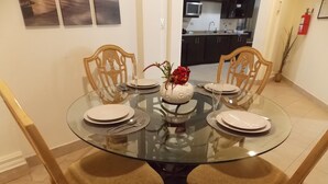 A round glass dining table with four chairs, a vase with flowers, and plates set for a meal.