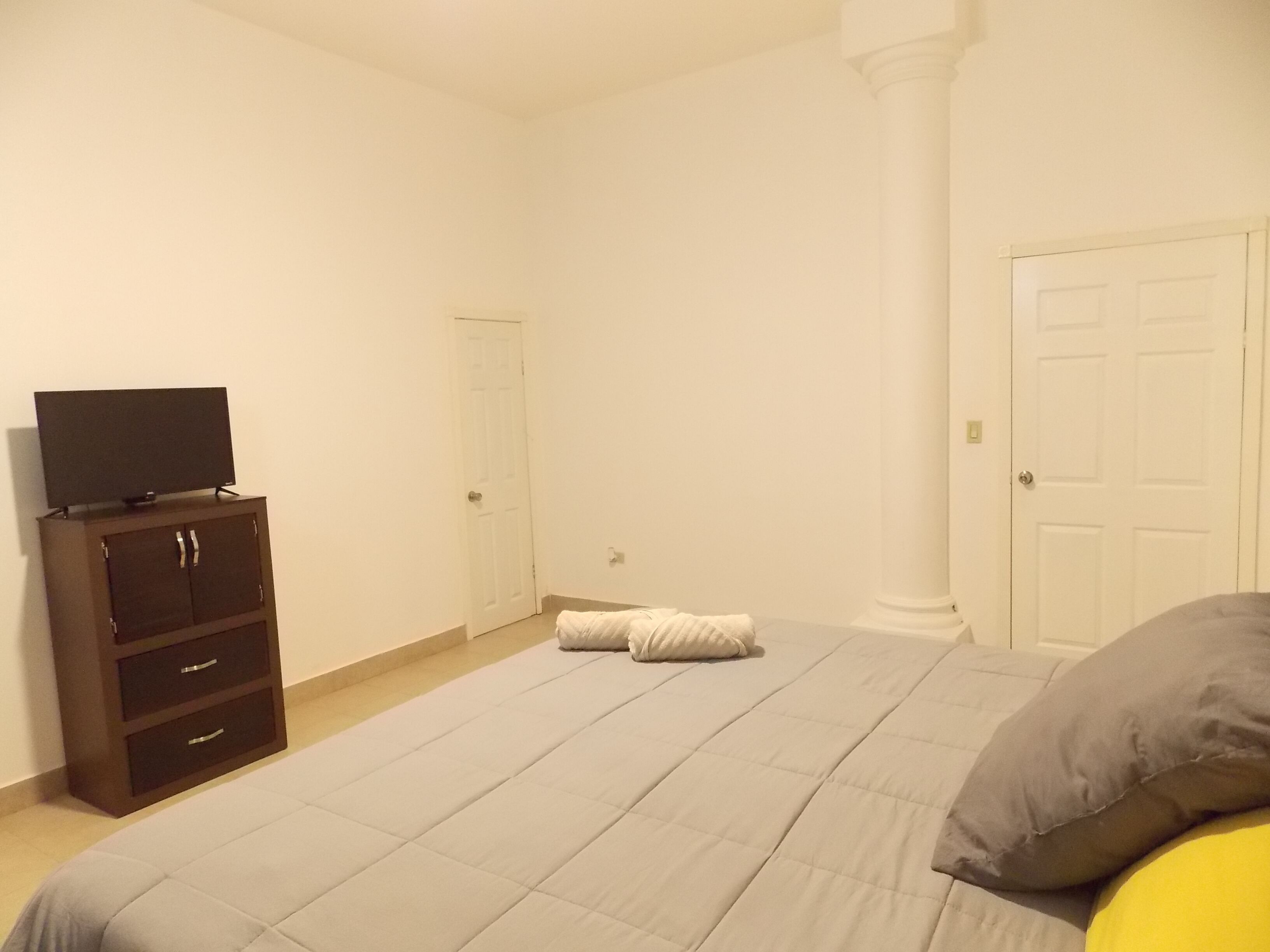 Ein Schlafzimmer mit einem Bett, einem Fernseher auf einer Kommode und zwei Türen.