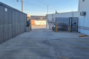 A parking area with a concrete floor, a metal fence on the left, and a building with a glass door on the right.