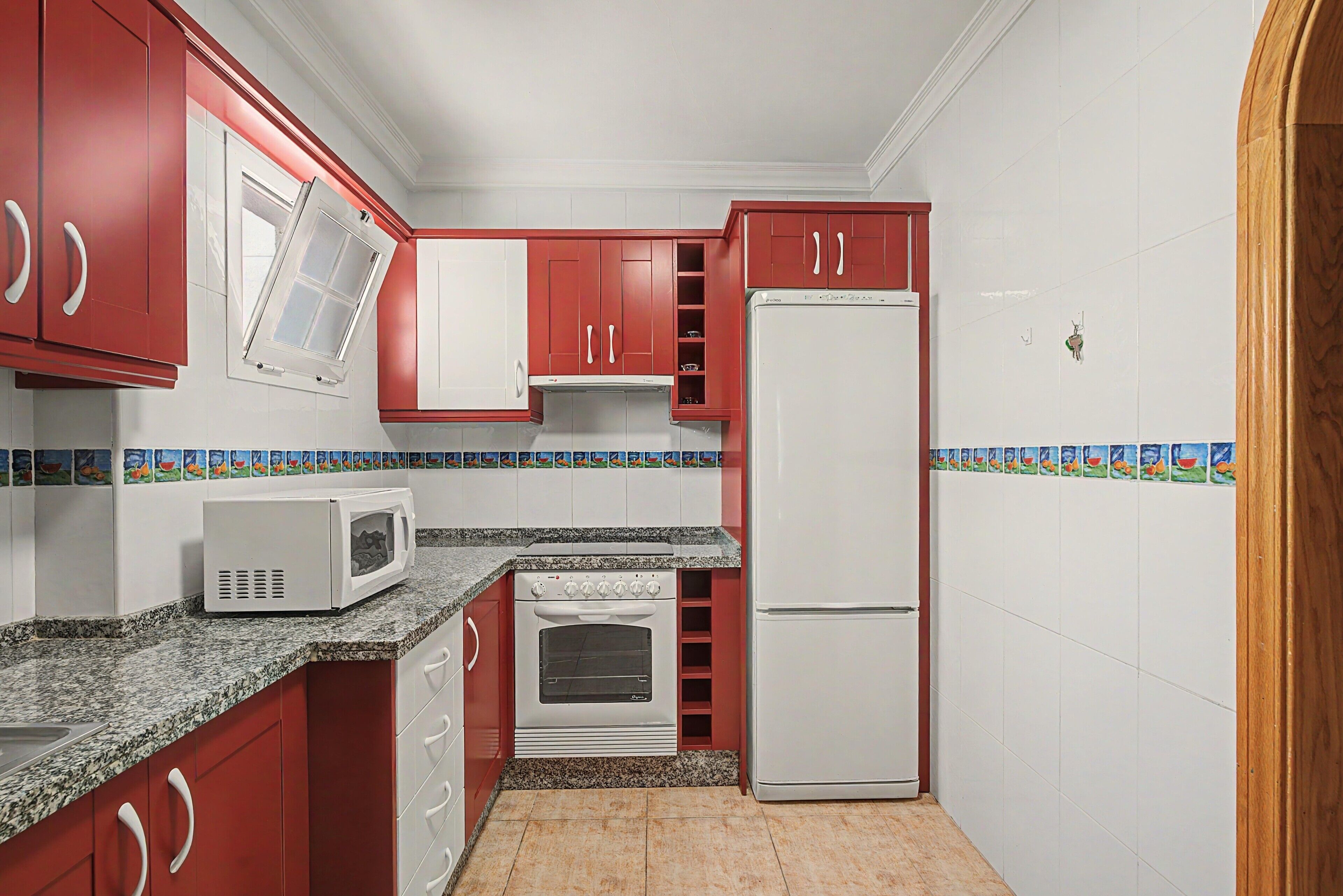 Eine Küche mit roten Schränken, einem weißen Kühlschrank, einer Mikrowelle und einem Backofen.