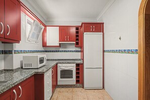 Una cocina con armarios rojos, un refrigerador blanco, un microondas y un horno.