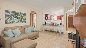 Ein Wohnzimmer mit einer Couch und Hocker, eine Küche mit roten Schränken und ein Essbereich mit weißen Stühlen.