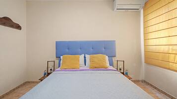 Un dormitorio con una cama, dos mesitas de noche, un equipo de aire acondicionado y una ventana con persianas.