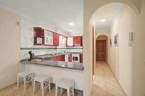 Eine Küche mit weißen Schränken, roten Akzenten, einer Arbeitsplatte aus Granit und einem eingebauten Backofen. Es sind drei weiße Hocker und ein kleiner Tisch vorhanden.
