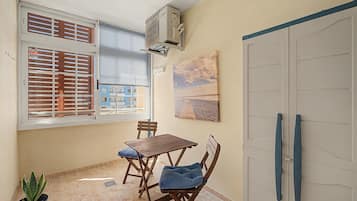 Un petit balcon avec une table et des chaises, un pot de fleurs et une vue sur les bâtiments environnants.