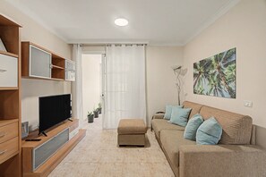 A living room with a flat-screen TV, wooden cabinets, a sofa with cushions, a painting on the wall, and a door leading to another room. - Vacation Apartment 'El Rincón De Ale' with Wi-Fi and Air Conditioning (Los Abrigos)