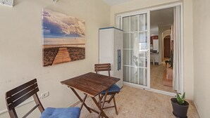 Ein kleiner Essbereich mit Tisch und Stühlen, ein Gemälde mit Strandmotiv sowie eine Glasschiebetür zum Küchenbereich.