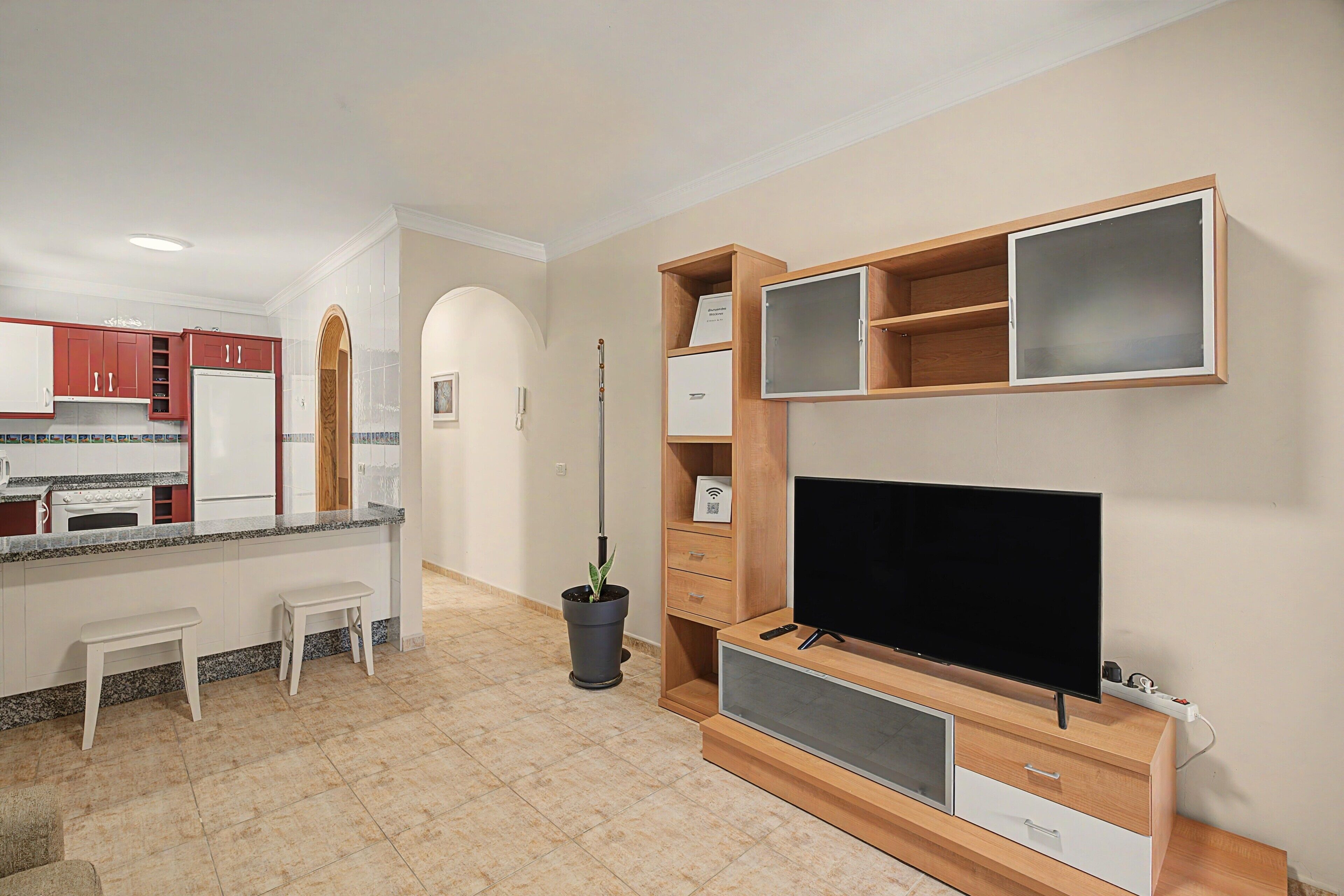 Eine moderne Küche mit Einbauofen, ein Essbereich mit weißem Tisch und Bank sowie ein Wohnbereich mit Flachbildfernseher und Holzböden.