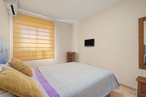 Un dormitorio con una cama, una ventana, un televisor y un armario de madera.