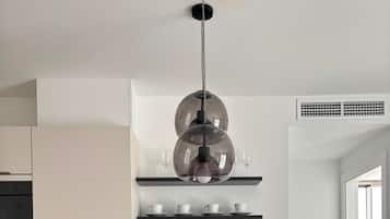 Une cuisine moderne avec un îlot central, des chaises rouges, un luminaire suspendu et une étagère intégrée où sont rangées des tasses et des verres.