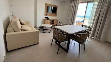 Un soggiorno moderno con un divano, un tavolo da pranzo con sedie, una TV a parete e vista mare attraverso ampie finestre.