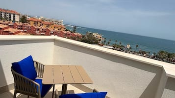 A terrace with a table and chairs, overlooking a coastal view with buildings and the sea.