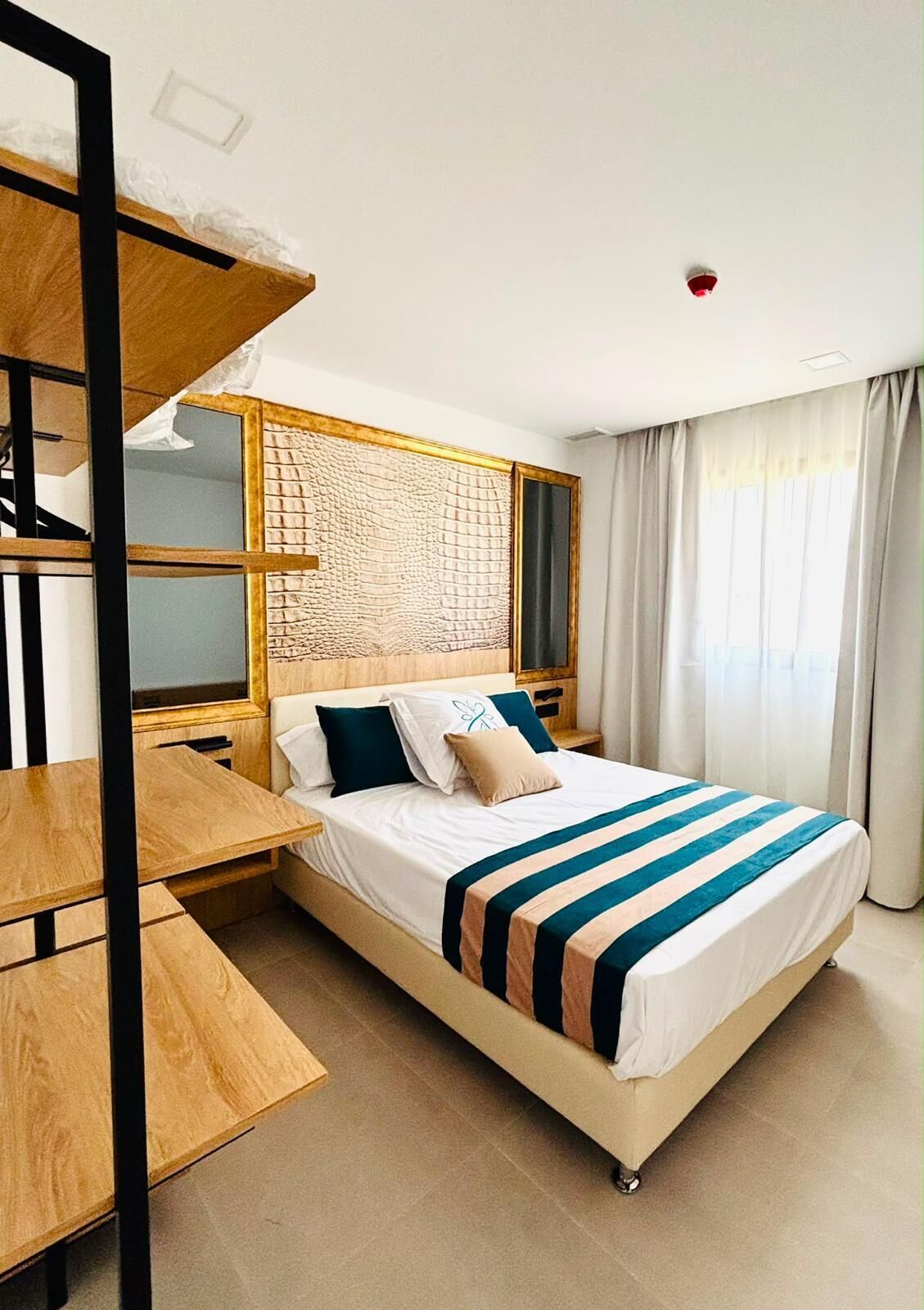 Ein modernes Hotelzimmer mit einem Bett, einem Holztisch und einer fest eingebauten Bücherreol.