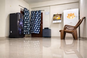 Una habitación con refrigerador, un armario, una silla, cortinas y una pared con un cartel.