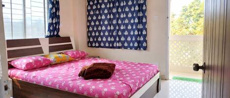 Un dormitorio con cama, almohadas, una ventana con cortinas y una puerta.