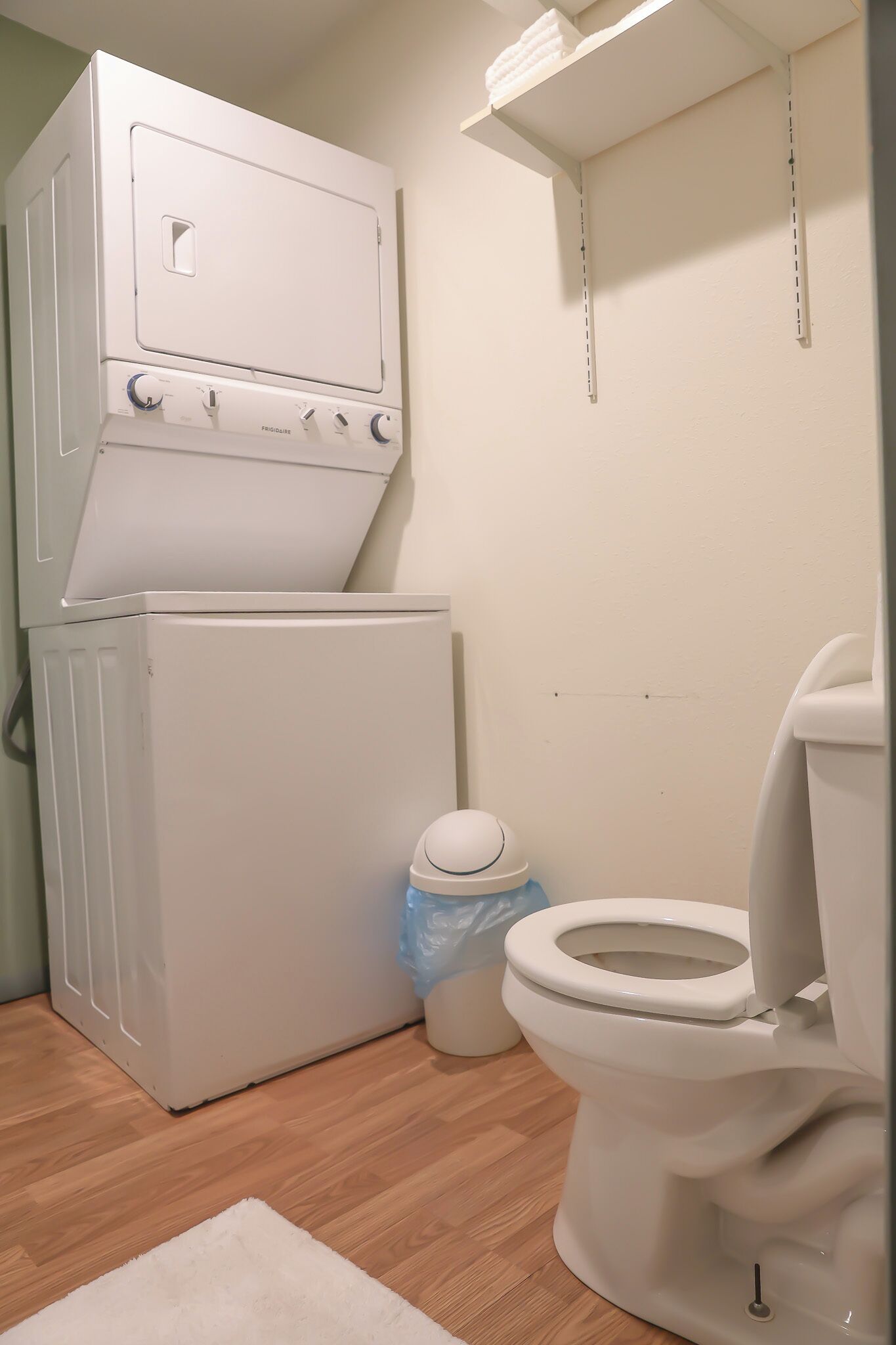 Ett litet badrum med en vit tvättmaskin, en toalett och en liten papperskorg.