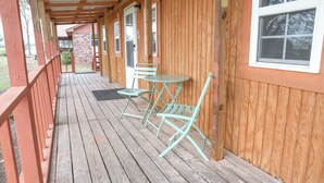 Terraza de madera con porche cubierto, una mesa y dos sillas.