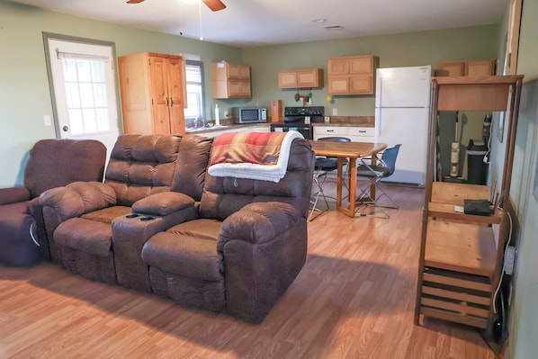 A living room with a sectional sofa, a dining table, and a kitchen area with wooden cabinets and appliances.